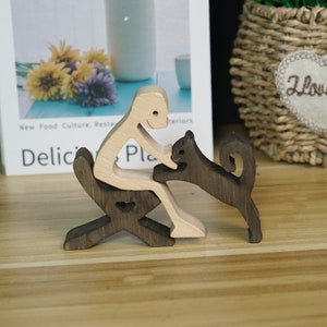 May include: Wooden figurine of a person sitting on a chair, reaching out to a wooden cat figurine. The person and chair are light brown, while the cat is dark brown.