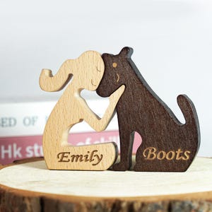 Könnte beinhalten: Holzfigur einer Mädchen und eines Hundes, beide mit personalisierten Namen. Das Mädchen ist aus hellem Holz und der Hund aus dunklem Holz. Das Mädchen kniet und der Hund sitzt. Der Name des Mädchens ist "Emily" und der Name des Hundes ist "Boots".