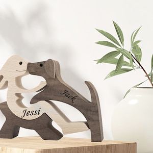 Könnte beinhalten: Holzskulptur von zwei Tieren, einem Kaninchen und einem Hund, die sich küssen. Das Kaninchen ist hellbraun und der Hund ist dunkelbraun. Das Kaninchen ist mit "Jessi" und der Hund mit "Jack" beschriftet.