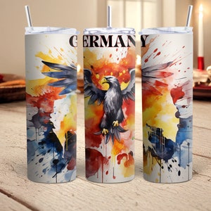 Peut inclure: Trois gobelets en acier inoxydable avec couvercles et pailles. Chaque gobelet présente un motif aquarelle d'un aigle allemand avec le mot "GERMANY" imprimé sur le devant. Le motif comprend des éclaboussures de jaune, orange, rouge, bleu et blanc.