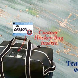 May include: Black hockey bag with white piping and a clear plastic window. The bag has a black handle and a name tag that says "#14 CARSON". Custom Hockey Bag Inserts.