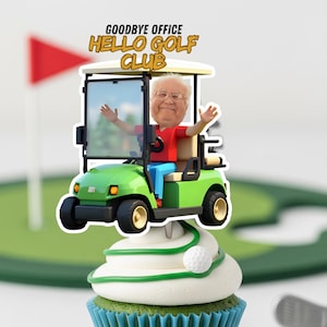 Puede incluir: Una magdalena con glaseado blanco y detalles verdes, coronada con una figura de carrito de golf. La figura muestra a una persona con una camisa roja y pantalones azules. El texto sobre el carrito dice "GOODBYE OFFICE HELLO GOLF CLUB". Una pelota de golf está en el glaseado.