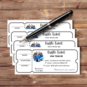 May include: A stack of white raffle tickets with a black pen on a wooden surface. Each ticket has a header that says "Raffle Ticket" and includes fields for name, telephone, and player information. The tickets feature a team photo.