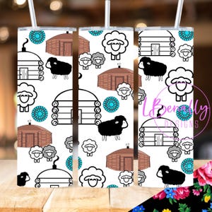 May include: White tumbler with a repeating pattern of black sheep, log cabins, and turquoise blue circles. The tumbler is designed for hot or cold beverages.