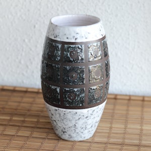 Peut inclure: Un vase en céramique blanche avec un motif géométrique brun et noir. Le vase a un glaçage blanc moucheté et une forme arrondie.