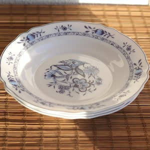 Könnte beinhalten: Eine weiße Suppenschüssel aus Keramik mit einem blauen und weißen Blumendesign. Die Schüssel hat einen gewellten Rand und ist mit einem zarten Blumenmuster verziert.