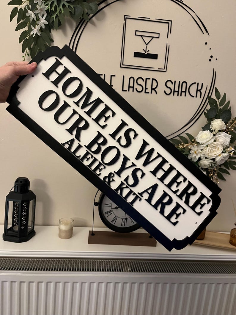 May include: Black and white wooden sign with the text "Home is where our boys are Alie & Kit".