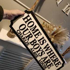 May include: Black and white sign with the text "Home is where our boys are" and the names Charlie, Albie, and Louie underneath.