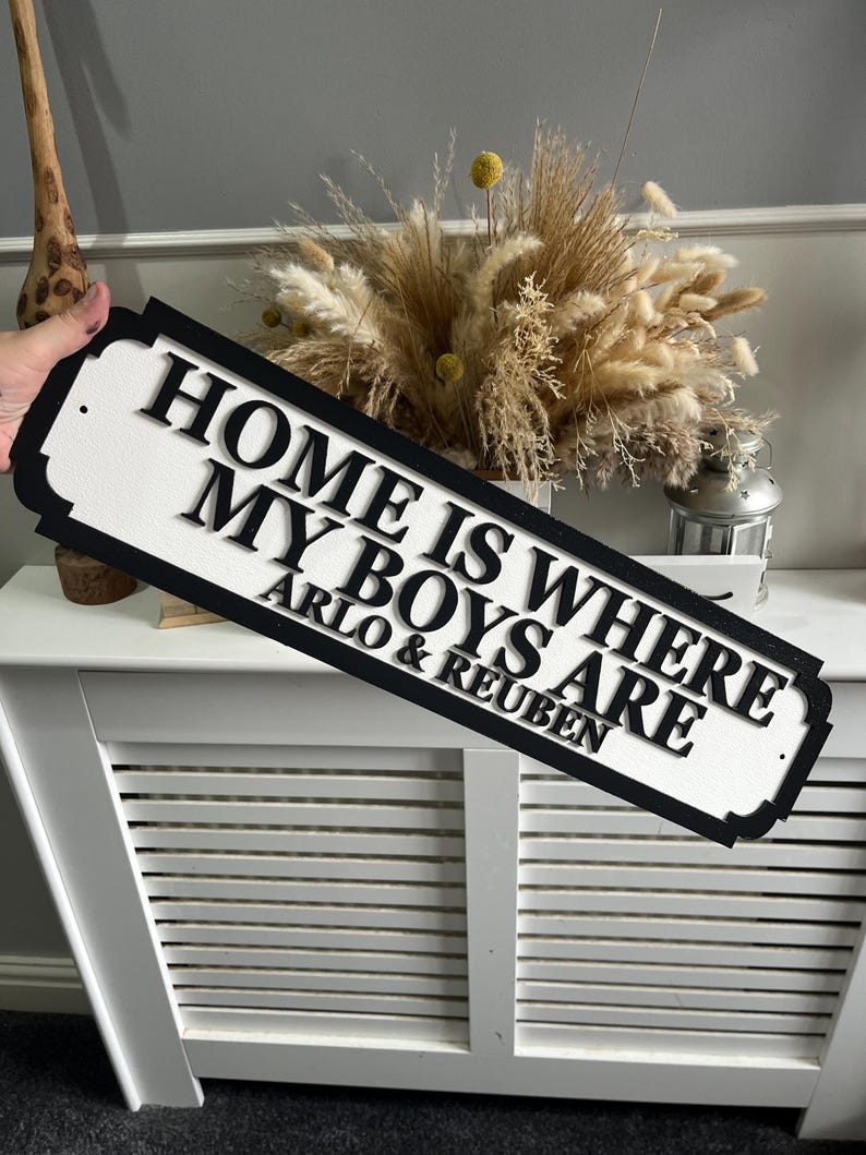 May include: White wooden sign with black lettering that reads "Home is where my boys are Arlo & Reuben".