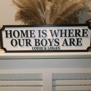 May include: Black and white wooden sign with the text "Home is where our boys are" and the names "Codie & Logan" underneath.