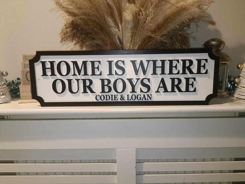 May include: Black and white wooden sign with the text "Home is where our boys are" and the names "Codie & Logan" underneath.