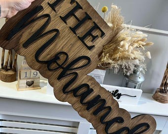 Può includere: Un cartello in legno con il testo "The Mohammads" in lettere nere. Il cartello è di colore marrone scuro e ha un aspetto rustico.