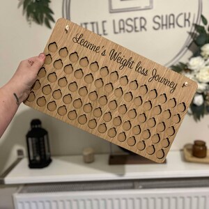 Może przedstawiać: Drewniany tracker utraty wagi ze 100 k&oacute;łkami do zaznaczania postęp&oacute;w. Tracker jest spersonalizowany tekstem "Leanne's Weight Loss Journey".