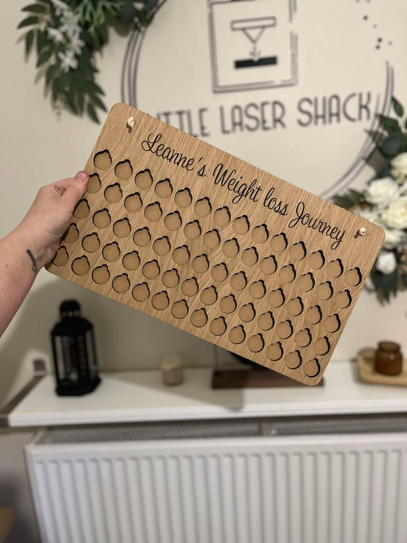 Może przedstawiać: Drewniany tracker utraty wagi ze 100 k&oacute;łkami do zaznaczania postęp&oacute;w. Tracker jest spersonalizowany tekstem "Leanne's Weight Loss Journey".