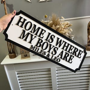 May include: Black and white wooden sign with the text "Home is where my boys are" and the names "Miles & Leo" below.