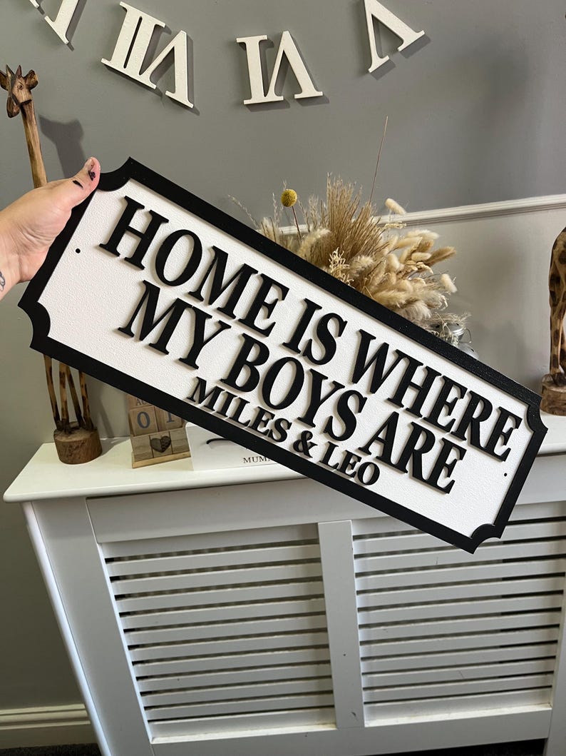 May include: Black and white wooden sign with the text "Home is where my boys are" and the names "Miles & Leo" below.