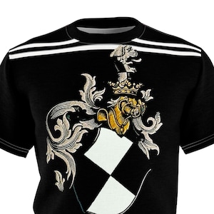 May include: Black t-shirt featuring a heraldic crest design. The crest includes a shield with a black and white diamond pattern, ornate scrollwork, and a golden lion. Two white stripes are across the top of the shirt.