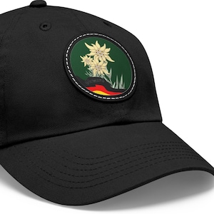 Könnte beinhalten: Eine schwarze Baseballkappe mit einem runden, grünen, weißen und gelben gestickten Aufnäher mit einer Blume und der deutschen Flagge.