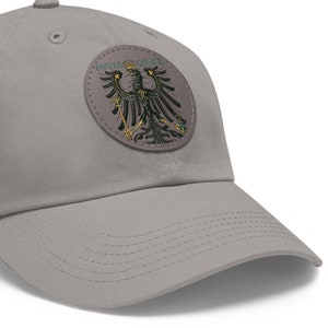 May include: A gray baseball cap with a round patch featuring a black eagle with gold accents and the text "SAUVVE QUI PEUT" in green.