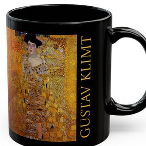 May include: Black ceramic mug with a gold and black image of a woman in a gold dress. The text "GUSTAV KLIMT" is printed on the side of the mug.