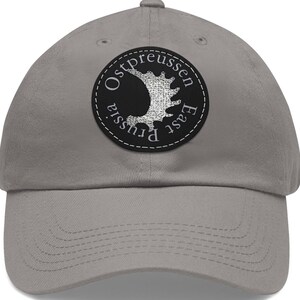May include: A gray baseball cap with a curved brim. The cap features a circular patch with the words "East Prussia" and "Ostpreussen" around a silver antler design on a black background.