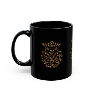 May include: Black ceramic mug with a gold design of a crown and a heart with a knot inside. The design is surrounded by thorns.