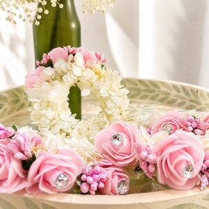 May include: A collection of floral garlands featuring cream-colored hydrangea petals and pink foam roses accented with small clear rhinestones in the center of each rose, alongside clusters of tiny pink buds arranged in a circular pattern.