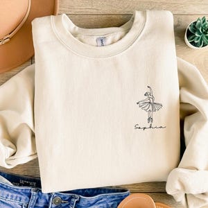 May include: A cream-colored sweatshirt with a black line drawing of a ballerina and the name "Sophia" printed on the front.
