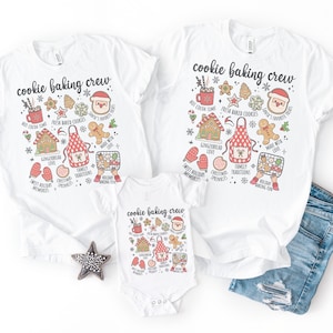 May include: Two white t-shirts and one white baby bodysuit featuring the text cookie baking crew. The graphic includes illustrations of a gingerbread house, a red apron, a mug of hot cocoa, a gingerbread man, and Santa Claus with text labels.