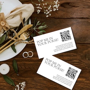 Può includere: Due carte bianche con testo nero e un codice QR su un tavolo di legno. Il testo sulle carte recita "Pop me in your purse!" e "Scansiona il nostro codice QR e carica le tue foto sul nostro album digitale. Non vediamo l'ora di vedere il nostro grande giorno dalla tua prospettiva!"