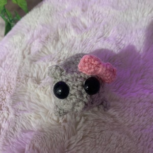 May include: A small grey crocheted stuffed animal with black eyes and a pink bow.