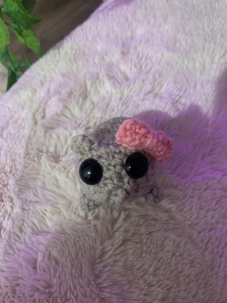 May include: A small grey crocheted stuffed animal with black eyes and a pink bow.