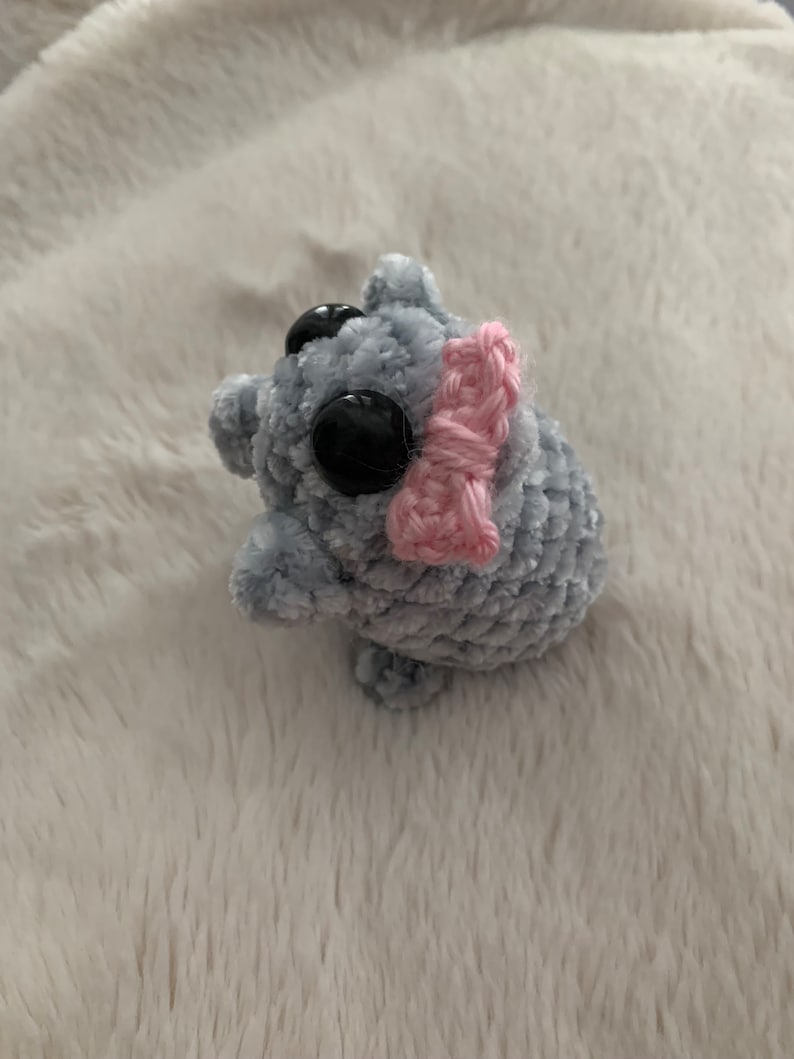 May include: A small grey crocheted plush toy with large black eyes and a pink crocheted bow.