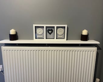 May include: A white shelf with two candles in black holders sits on top of a white radiator. The shelf is decorated with a white picture frame with three black and white paw prints and the words "Sleep Well" and "Forever In My Heart".