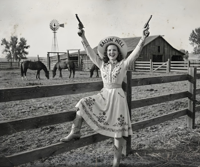 A vintage style black and white photograph of a smiling cowgirl standing with one boot propped on a wooden fence. She is triumphantly holding two revolvers in the air, and the underside of her cowboy hat reads "RAISIN' HELL". A classic ranch scene with horses, a windmill, and a wooden barn is in the background.