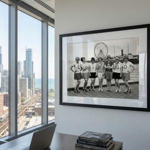 May include: A framed black and white photograph of seven women in matching outfits posing on a pier. The women wear skirts and shirts with the letters "C", "H", "I", "C", "A", and "G", "O". A Ferris wheel and a ship are visible in the background.