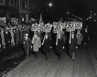 May include: Black and white photograph of a nighttime protest. A group of men march down a street holding signs that read "WE WANT BEER." An American flag is visible, and a crowd of people watches from the sidewalk.