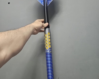 May include: A blue and yellow dart with a black shaft and blue and white flight. The flight has a honeycomb pattern and the word "OCKY" printed on it. The dart is held against a gray background.