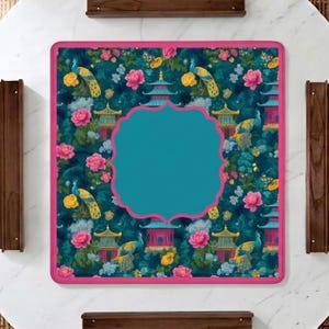 Op de afbeelding: Een vierkante deken met een donkergroenblauwe achtergrond met een herhalend patroon van pauwen, pagodes en roze en gele bloemen. Een groot, effen groenblauw kader met geschulpte randen is in het midden geplaatst, afgezet met een felroze bies.