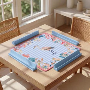 May include: A square puzzle mat featuring a light blue and white striped background with a central heron illustration surrounded by a border of colorful sea creatures including crabs, lobsters, and starfish, framed by four light blue plastic rails.