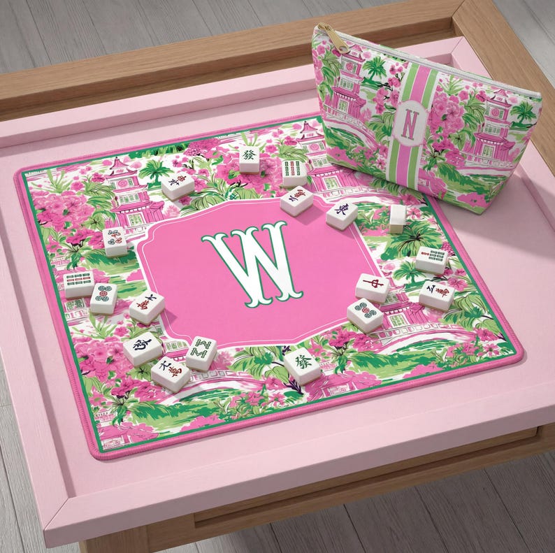 May include: A pink and green Mahjong set with a matching cosmetic bag. The set includes a pink mat with a large white "W" in the center, surrounded by Mahjong tiles. The bag and mat feature a floral and pagoda design.