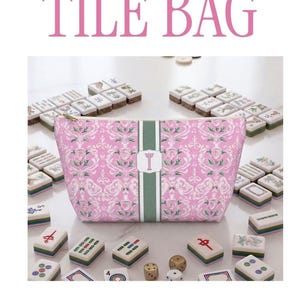 May include: A pink and white damask patterned pouch and tote bag set featuring a central vertical green stripe with a white monogrammed label. The bags have gold-toned zippers or rope handles and are displayed with mahjong tiles and dice.