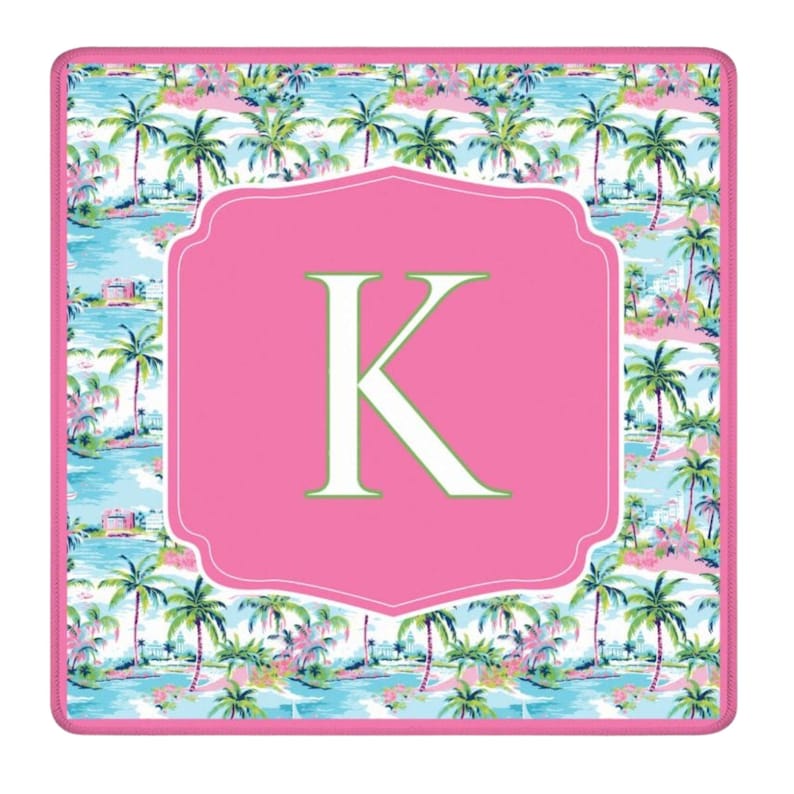 May include: A square, decorative mousepad featuring a tropical scene with palm trees, water, and buildings. A pink, scalloped frame surrounds a large, white letter "K" on a pink background. The border is pink.