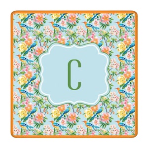 Puede incluir: Alfombra decorativa cuadrada con un estampado floral y de p&aacute;jaros en tonos azules, naranjas, amarillos y rosas. Un centro azul claro presenta la letra verde "C" dentro de un borde festoneado blanco. La alfombra tiene un borde naranja.