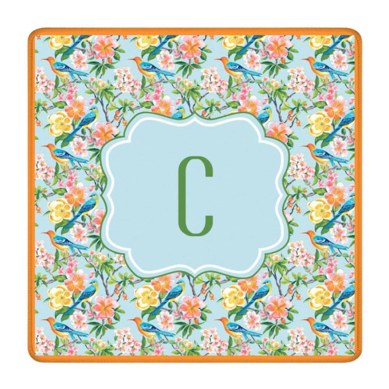 Puede incluir: Alfombra decorativa cuadrada con un estampado floral y de p&aacute;jaros en tonos azules, naranjas, amarillos y rosas. Un centro azul claro presenta la letra verde "C" dentro de un borde festoneado blanco. La alfombra tiene un borde naranja.