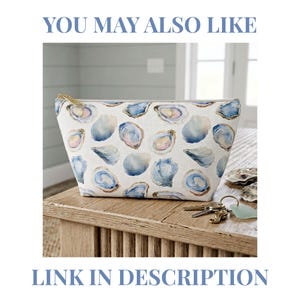 May include: A zippered pouch featuring a repeating watercolor print of blue and white oyster shells on a light background. The pouch has a gold-toned metal zipper pull and is positioned on a wooden surface with a set of keys nearby.