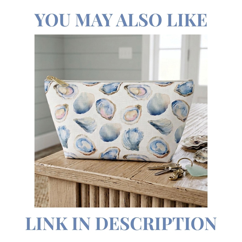 May include: A zippered pouch featuring a repeating watercolor print of blue and white oyster shells on a light background. The pouch has a gold-toned metal zipper pull and is positioned on a wooden surface with a set of keys nearby.
