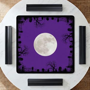 K&ouml;nnte beinhalten: Eine quadratische Spielmatte mit einem leuchtend violetten Hintergrund und einem gro&szlig;en, zentrierten Vollmond. Der Rand ist mit einer schwarzen Silhouette eines Friedhofs verziert, die Grabsteine, kahle B&auml;ume und Eisenz&auml;une zeigt.