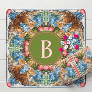 May include: A decorative square mat with a leopard print border and a central green circle featuring the letter "B". The mat includes pink flowers, blue vases, and a matching pencil case with the letter "B".