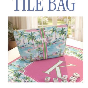 May include: A zippered pouch and a tote bag featuring a tropical palm tree and coastal building print in shades of blue, pink, and green. Both items have a central vertical green and pink stripe with a white monogram letter and white rope handles.